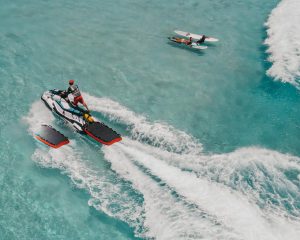 Experience the thrill of jet skiing on turquoise Hawaiian waters with surfers nearby.